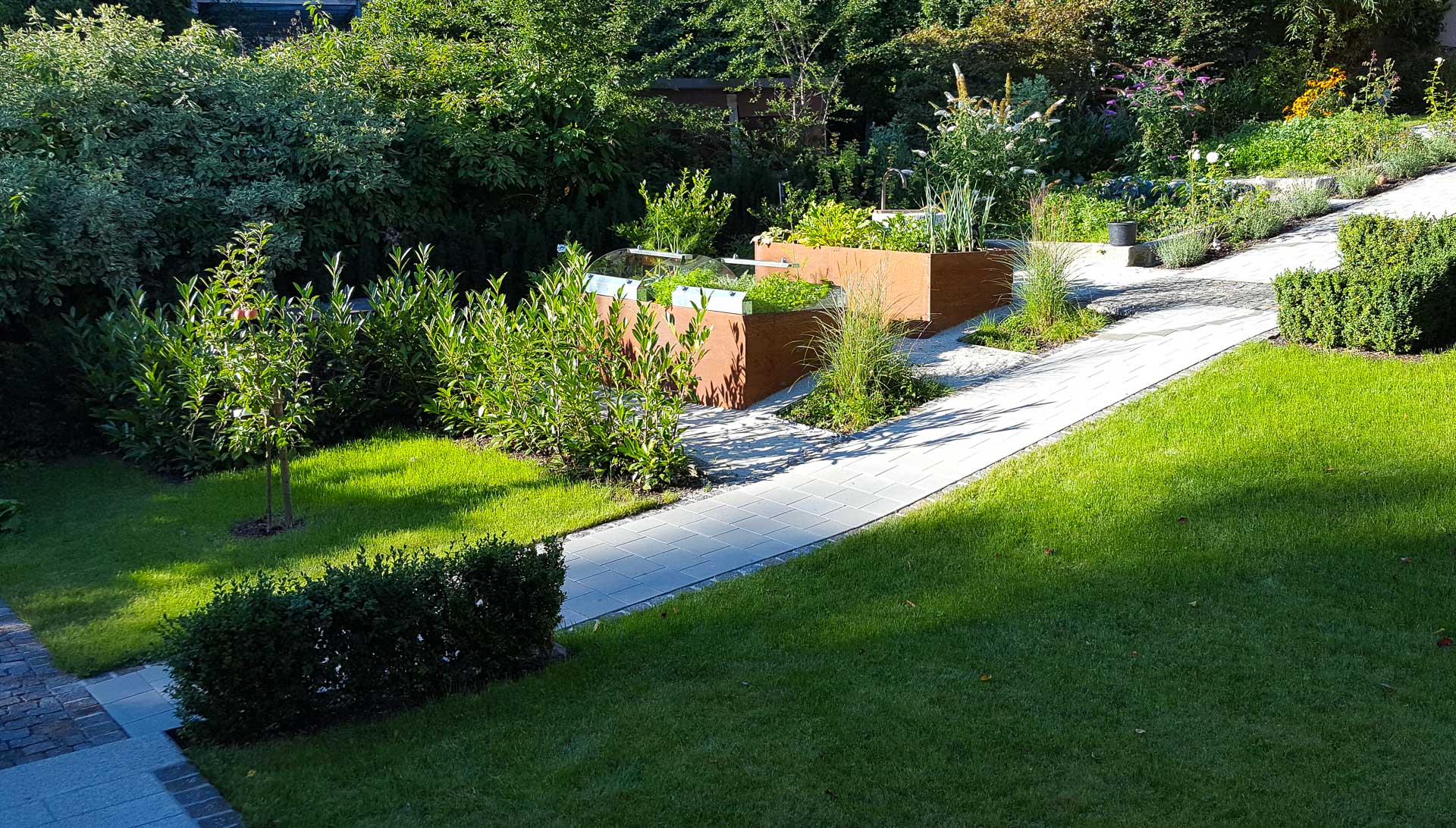Garten mit grünen Hochbeeten aus Holz, gepflegtem Rasen, Sträuchern und bepflastertem Gehweg